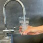 Eine Hand hält unter einem offenen Wasserhahn ein Glas und füllt es mit Trinkwasser.